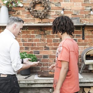 Dr Copley in a white shirt and black jeans talking to a teenage member of the Sourdough Club about pizza