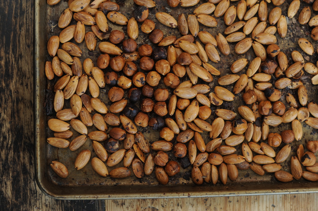 Top view of a baking tray filled with roasted almonds and hazelnuts, showcasing their golden-brown colour and rustic appearance.